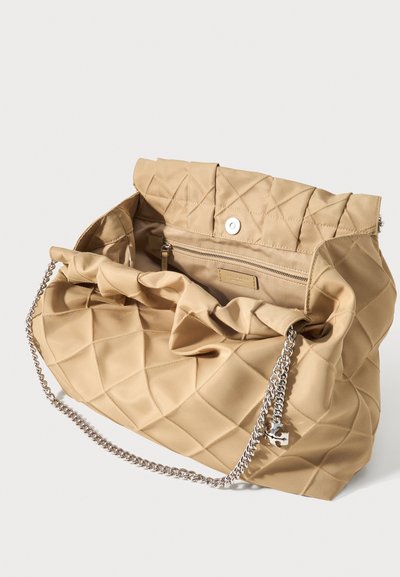 Μπεζ τσάντα με καπιτονέ σχέδιο, πτυσσόμενο καπάκι, κλείσιμο με μαγνητικό κουμπί, εσωτερική τσέπη με φερμουάρ και αλυσίδα από ασημί για τον ώμο.