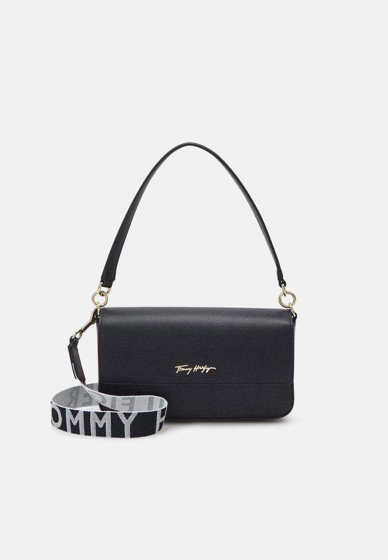 Sac à bandoulière rectangulaire noir en cuir avec logo doré et une large bandoulière en tissu amovible imprimée de "Tommy Hilfiger" en noir et blanc.