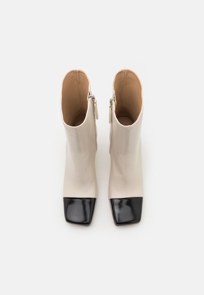 Beige leren enkellaarsjes met zwarte lakvierkante neus, met een strak ontwerp en een ritssluiting aan de zijkant. Gladde textuur over het geheel.