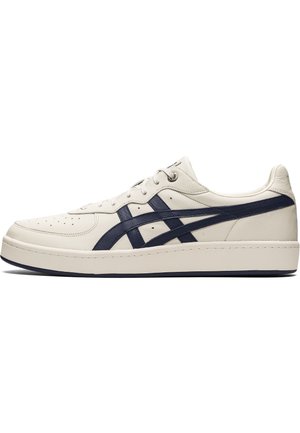 White leather sneaker with navy accents, featuring perforated upper for breathability, flat laces, and a thick rubber sole.