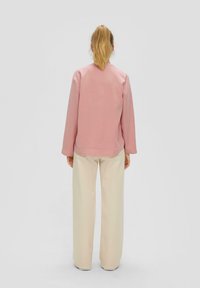 Lichtroze lange mouw top gezien vanaf de achterkant, gecombineerd met een losse beige broek. Soepele textuur, eenvoudig design en geen zichtbare patronen.