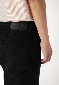 Jeans de mezclilla negros con un acabado texturizado, que presentan una etiqueta de cuero con la inscripción "ONLY & SONS" en la cinturilla y bolsillos traseros en ángulo.