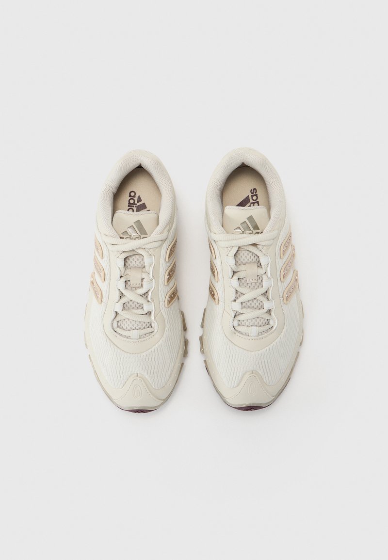 Lys beige idrettssko med mesh- og syntetisk overdel, med tre brune striper, snøring og en teksturert såle.
