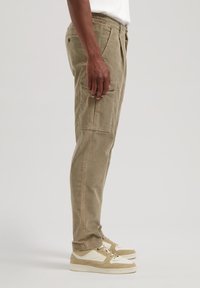 Beige kordfløyelsbukser med smal passform, med sidelommer og elastisk liv, sammen med beige og hvite sneakers.