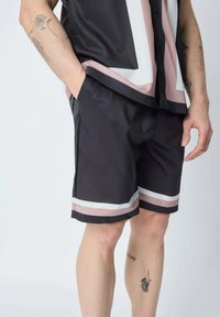 Shorts en satin noir avec des rayures horizontales roses et blanches. Comprend des poches latérales et une texture légère et lisse. Tatouage visible sur la jambe.