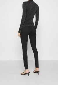 Czarna bluzka z długim rękawem o subtelnym połysku, dopasowany krój; w połączeniu z czarnymi obcisłymi jeansami i sandałami na obcasie z odkrytymi palcami.