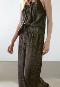 Combinaison noire sans manches, présentant une coupe décontractée, une taille élastique et un motif texturé. Le tissu se drape doucement, mettant en valeur la silhouette générale.