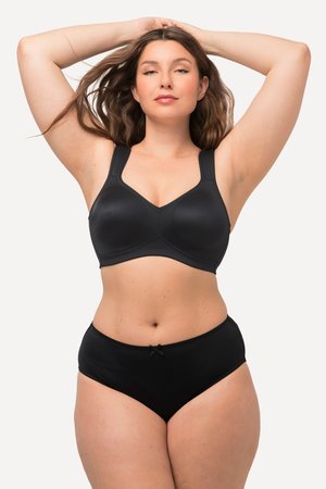 Frau mit langen braunen Haaren, die einen schwarzen BH und passende schwarze Unterwäsche trägt, steht mit erhobenen Armen vor einem schlichten hellen Hintergrund.