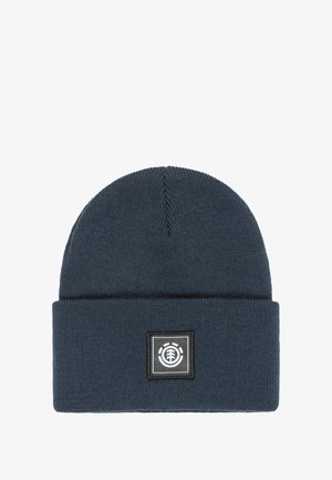 Gorro de punto de color azul oscuro con puño doblado, que presenta un parche de logo cuadrado con acentos en blanco y negro. Textura suave, parte superior redonda.