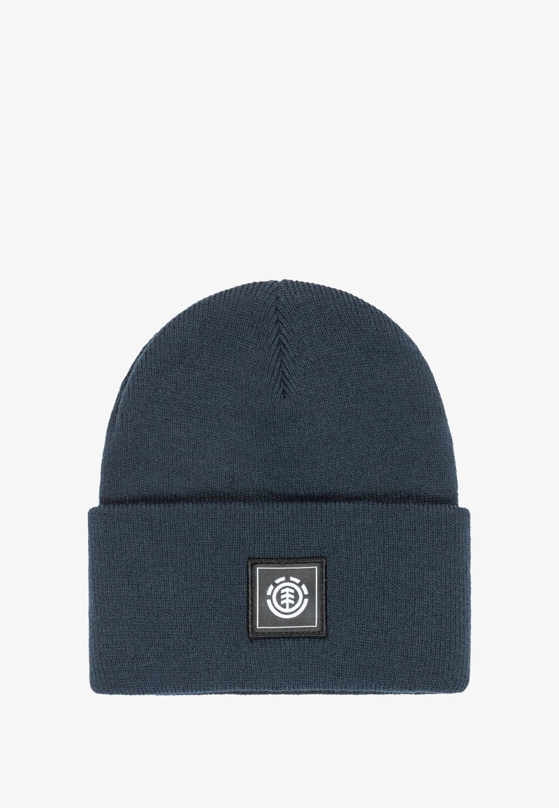 Donkerblauwe gebreide beanie met een omgevouwen rand, voorzien van een vierkante logo-label met zwart-witte accenten. Zachte textuur, ronde bovenkant.