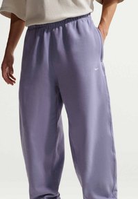 Pantalon de survêtement violet en tissu doux, avec une ceinture élastique, des poches latérales et un petit logo Nike blanc sur la cuisse gauche.