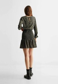 Black floral dress with long sleeves, fitted bodice, ruffled hem, and keyhole back detail. Paired with black ankle boots.