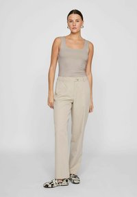Beige tailored trousers with a button closure, paired with a light taupe fitted tank top. Features a square neckline and plain texture.