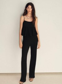 Top peplum negru fără mâneci, cu bretele subțiri, asortat cu pantaloni negri texturați, ajustați. Modelul poartă sandale cu bretele și un colier din argint.