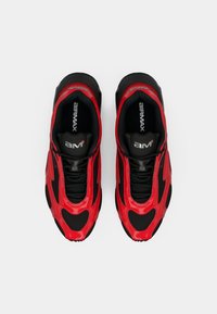 Las zapatillas deportivas rojas y negras presentan un upper liso con un diseño de onda, paneles de malla y cordones negros. Logo "AIRMAX" visible en la lengüeta.
