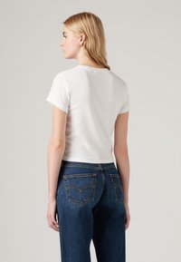 Balta, trumpomis rankovėmis marškinėliai su prigludusia forma. Suderinti su tamsiai mėlynomis, aukštu liemeniu džinsais, turinčiais dvi užpakalines kišenių ir siuvinėjimo akcentus.