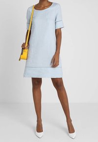 Ljusblå klänning med korta ärmar, rund halsringning och rak skärning. Har dekorativ sömnad och är kombinerad med en gul axelväska.