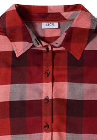 Chemise à carreaux rouges et roses avec boutons, col pointu et étiquette "CECIL" à l'intérieur de l'encolure.