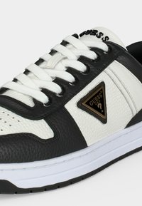 Baskets en cuir noir et blanc avec lacets blancs, un logo triangulaire Guess sur le côté et le marquage "Guess" sur la languette.