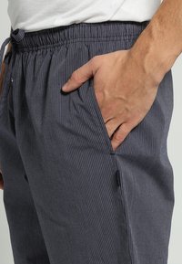 Marine gestreepte broek met elastische tailleband, trekkoord en zijzak. De stof heeft een zachte textuur en vertoont dunne verticale lijnen door het geheel.