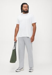 White cotton t-shirt, gray sweatpants, holding a green fabric tote bag, wearing gray and white athletic shoes. Short sleeves, relaxed fit.