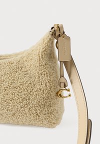 Plecu soma krēmkrāsā ar vilnai līdzīgu tekstūru virspusē. Aprīkota ar zelta toni sprādzi un ādas siksnu ar pievienotu zīmola etiķeti.