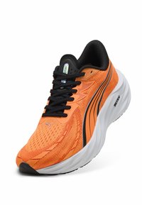 Zapatilla deportiva de correr en naranja y negro con suela blanca, cordones negros y parte superior de malla texturizada, en ángulo para mostrar detalles frontales y laterales.
