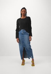 Zwarte geribbelde langefsleevetop, hoge taille spijker maxi rok met een zijopening, gecombineerd met groene sandalen met bandjes.