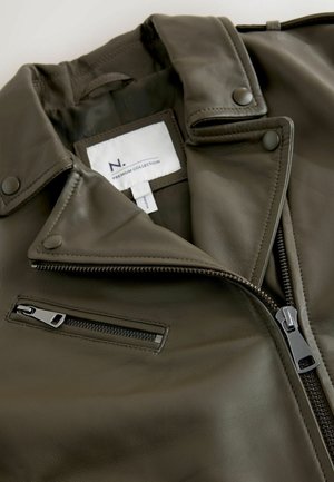 Veste de moto en cuir vert olive avec un col en V, une fermeture éclair à l'avant et une poche latérale. Comprend une étiquette de marque et une texture lisse.