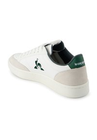 Białe i beżowe skórzane sneakersy z zielonym logo i zakładką na pięcie, niski fason, sznurowadła i biała gumowa podeszwa.