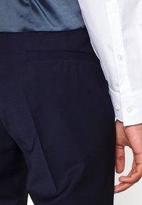 Witte overhemd met knopenmanchetten, gecombineerd met donkerblauwe maatwerkbroek, met een slank ontwerp en een gladde stoftextuur.