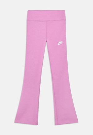 Rožnate ženske gamaše Nike z razširjenimi hlačnicami, visokim pasom in belim logotipom Nike na zgornjem levem stegenu, položene na ravno belo podlago.