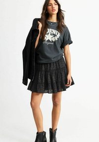Svart denimjacka, grå grafisk t-shirt med blommönster, lager-på-lager svart volangmini kjol och ankelstövlar med nitar.