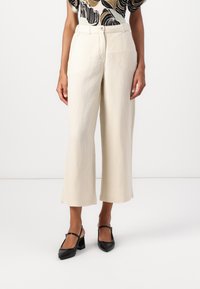 Pantaloni beige a gamba larga realizzati in un tessuto leggero, con vita alta e una sottile trama del tessuto, abbinati a scarpe nere con tacco a blocco.