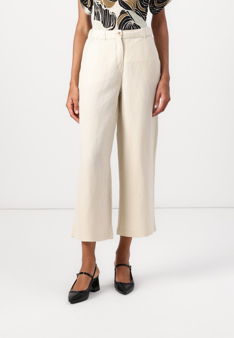 Pantaloni beige a gamba larga realizzati in un tessuto leggero, con vita alta e una sottile trama del tessuto, abbinati a scarpe nere con tacco a blocco.
