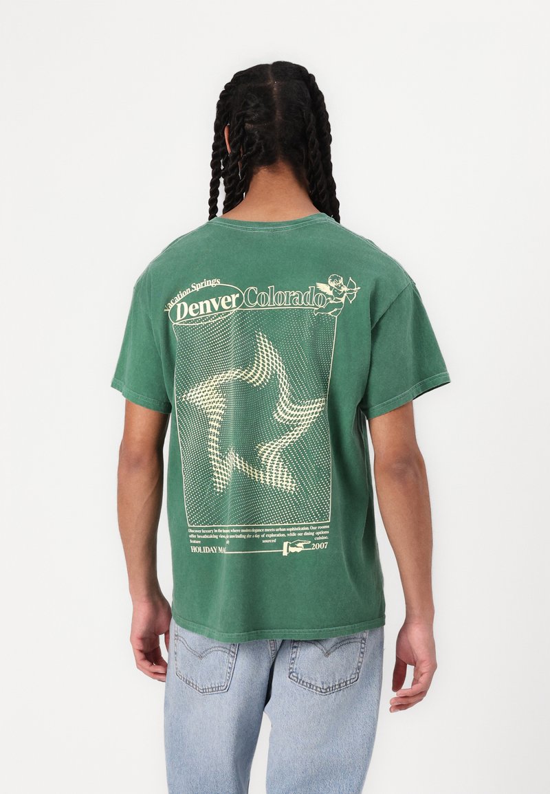 Groene katoenen t-shirt met een grafisch ontwerp van een sterrenpatroon en de tekst "Denver Colorado" in het geel op de achterkant. Korte mouwen en een comfortabele pasvorm.