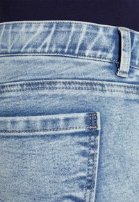 Jeans de mezclilla azul claro con un diseño de pierna recta, costuras de bolsillo visibles y una ligera textura desgastada cerca de la cintura.
