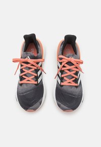 Sport schoenen met een gestructureerde donkergrijze bovenkant, zwart-witte strepen, roze veters en een witte tussenzool. Accentuatie aan de hiel in lichtroze.