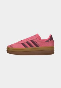Ροζ αθλητικό παπούτσι Adidas Gazelle με σκούρες ροζ ρίγες, διακοσμητική λεπτομέρεια στη μύτη και παχιά, τριπλή στρώση καφέ σόλας σε λευκό φόντο.