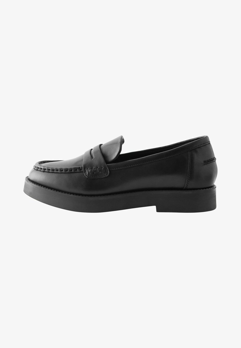 Mocassins en cuir noir avec une semelle plate, un bout rond et des coutures décoratives sur le dessus. Pas de quincaillerie ni de motifs visibles.