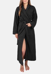 Schwarzer Bademantel mit langen Ärmeln, Taillenkordel und seitlichem Schlitz. Aus Frottee-Material gefertigt, mit einer Vorderseite-Tasche. Weicher Stoff.