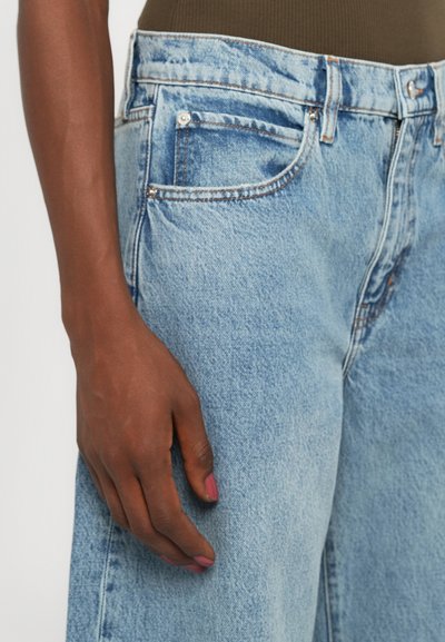 Jeans in denim azzurro chiaro con vestibilità rilassata, cinque tasche e cuciture arancioni. Il tessuto presenta una leggera texture consumata.