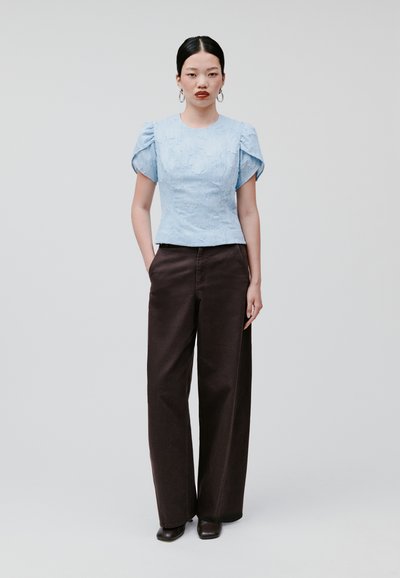 Top azzurro chiaro con texture e maniche a sbuffo abbinato a pantaloni larghi marroni scuri. L'outfit presenta una vestibilità su misura con tasche laterali.