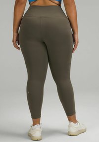Olijfgroene leggings met een hoge taille en een gladde, rekbare textuur, gecombineerd met beige sportschoenen met lichte accenten.
