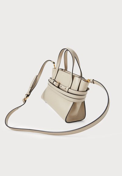 Sac à main en cuir beige à la forme structurée, avec deux poignées supérieures et une bandoulière amovible. Il présente des bords noirs et un accent ceinturé.