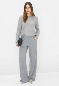 Lichtgrijze, losgebreide trui met ribbels aan de manchetten, gecombineerd met wijde grijze ribbroek. Model houdt een kleine zwarte tas vast en draagt zilveren schoenen.