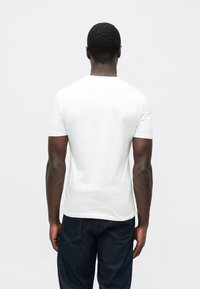 Άσπρο κοντομάνικο βαμβακερό μπλουζάκι με στρογγυλή λαιμόκοψη και απαλή υφή. Φορεμένο με σκούρο τζιν παντελόνι.