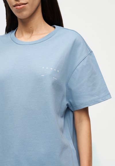 Ανοιχτό μπλε βαμβακερό T-shirt με στρογγυλή λαιμόκοψη, κοντά μανίκια και λευκό τυπωμένο λογότυπο στο στήθος. Μαλακή υφή, άνετη εφαρμογή.