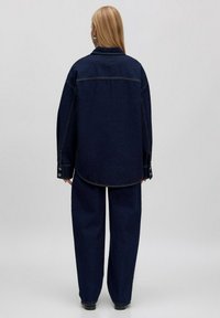 Donkerblauwe spijkerjacket met lange mouwen, grote kraag en knoopmanchetten. Ruimvallend, gecombineerd met wijde spijkerbroeken.