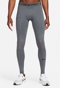 Leggings Nike Pro grises con un diseño ajustado, que incluyen un bolsillo lateral, paneles en contraste y una cinturilla con la marca.